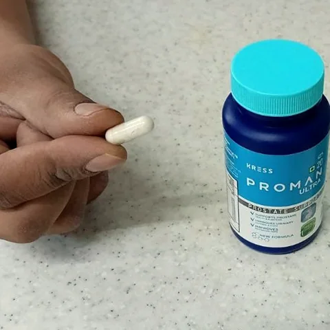 Hand holding a white Proman capsule next to the Proman Ultra bottle